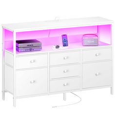 a white dresser with pink lights and electronics on it's top shelf, next to a remote control