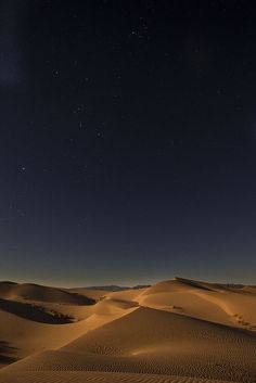 the night sky is lit up over sand dunes