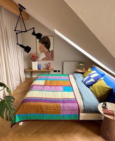 a bed with colorful blankets and pillows on top of it next to a window in an attic