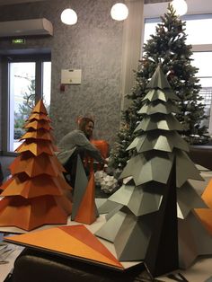 a woman sitting in front of a christmas tree made out of folded origami