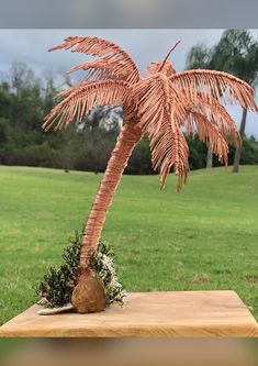 a pink palm tree sitting on top of a wooden table next to a lush green field