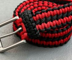 a red and black braided belt with metal buckles on a gray surface,