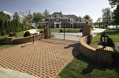 a brick driveway leading to a large house with a gate and light post in the middle