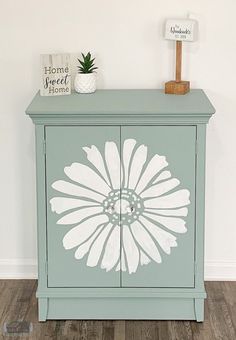 a blue cabinet with white flowers painted on the front and sides, sitting against a wall