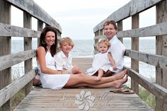 a family sitting on a wooden bridge by the ocean