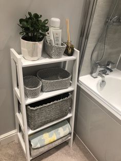 a white shelf with baskets and towels on it next to a bathtub in a bathroom