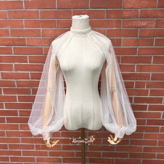 a mannequin wearing a white dress with sheer sleeves on display in front of a brick wall