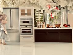 a doll is standing in front of a kitchen with flowers on the wall and cabinets