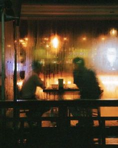 two people sitting at a table in front of a window with rain falling down on them