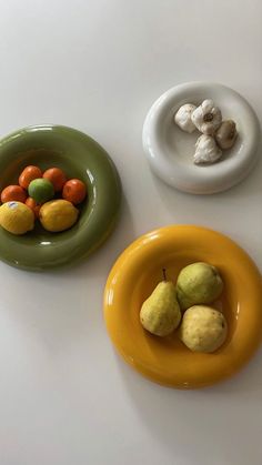 three bowls with fruit in them sitting on a white table next to some mushrooms and oranges