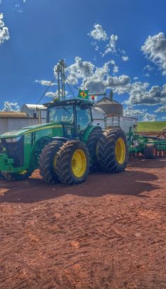 a green tractor parked in front of a farm building with two silos on the other side