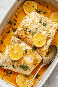 two fish fillets in a white dish with lemons and parsley