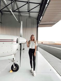 a woman standing next to an airplane in a hang - off hangar with her hand on the wing