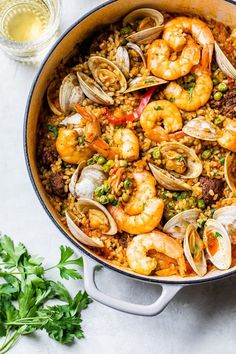 a pan filled with seafood and rice next to parsley on the side, along with a glass of water