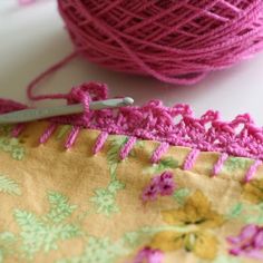 a pink ball of yarn sitting next to a pair of scissors on top of a piece of fabric