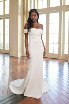 a woman in a white wedding dress standing on a wooden floor with large windows behind her