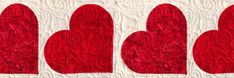 three red heart shaped pieces on a white quilted wall hanging from the side of a window