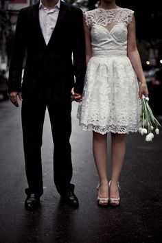 a man and woman are holding hands while walking down the street with flowers in their hand