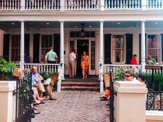 people are sitting on the front porch of a white house with columns and balconies