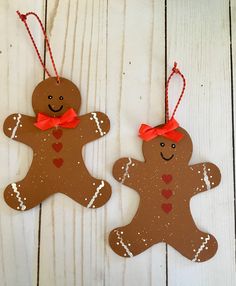 two homemade gingerbread cut out ornaments hanging on a white wooden background with red ribbon