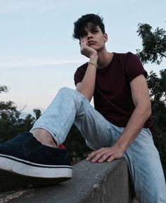 a young man sitting on top of a cement wall with his hand under his chin