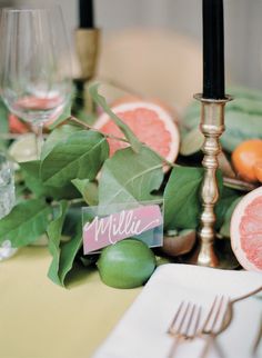 the table is set with grapefruits, oranges and silverware