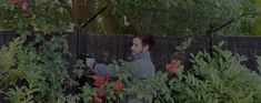 a man holding a camera in front of some bushes and trees with red flowers on it