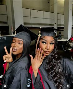 two young women in graduation gowns posing for the camera with their fingers up and one holding