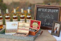 an assortment of liquor bottles and cigars on a table with a chalkboard sign