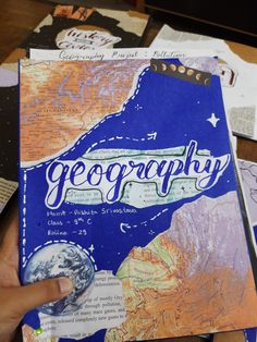 a person holding up a book with the word geography on it, surrounded by other books