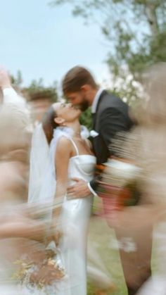 a blurry photo of a bride and groom kissing in front of an outdoor crowd