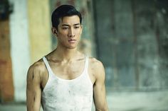 a man in white tank top standing next to a building with graffiti on it's walls