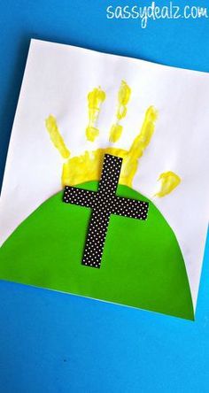 a handprinted cross on top of a green hill with yellow hands and dots