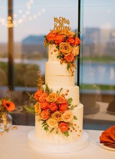 a three tiered cake with orange flowers on the top is sitting on a table in front of a window