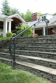 a stone wall and metal handrail in front of a house