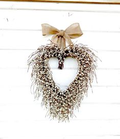 a heart shaped wreath hanging on the side of a white building with a bow around it