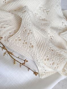 a white knitted blanket laying on top of a bed next to a flower vase