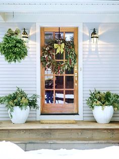 three potted plants are sitting on the front step of a white house with a wooden door