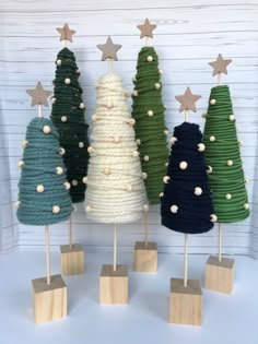 three small christmas trees on wooden stands with stars and yarn wrapped around the top, all in different colors