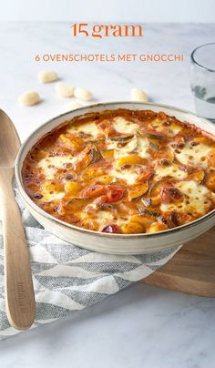 a pizza with cheese and tomatoes in a pan on a cutting board next to a glass of water