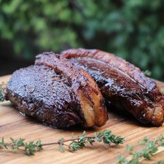 two pieces of meat sitting on top of a wooden cutting board next to green plants