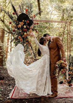 a bride and groom kissing in front of an arch decorated with flowers, leaves and foliage