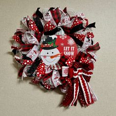 a red and white christmas wreath with a snowman decoration on the top, says let it snow