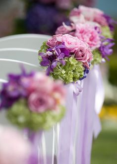 purple and green flowers are tied to white chairs