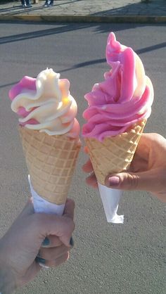 two ice cream cones with pink and white icing are being held by someone's hand