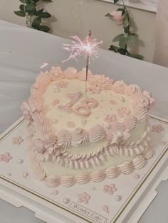 a pink and white birthday cake with a sparkler on top, sitting on a table