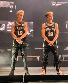 two young men standing on top of a stage wearing black and white shirts with silver numbers