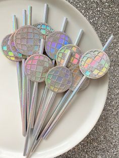 six holographic stir sticks on a white plate with silver and iridescent colors