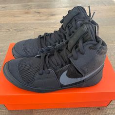 a pair of black and grey nike shoes on an orange box with wood flooring