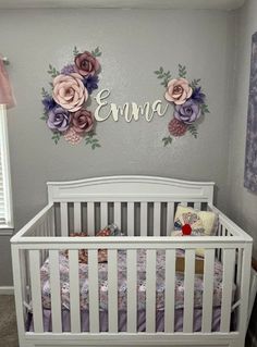 a white crib with pink and purple flowers on the wall